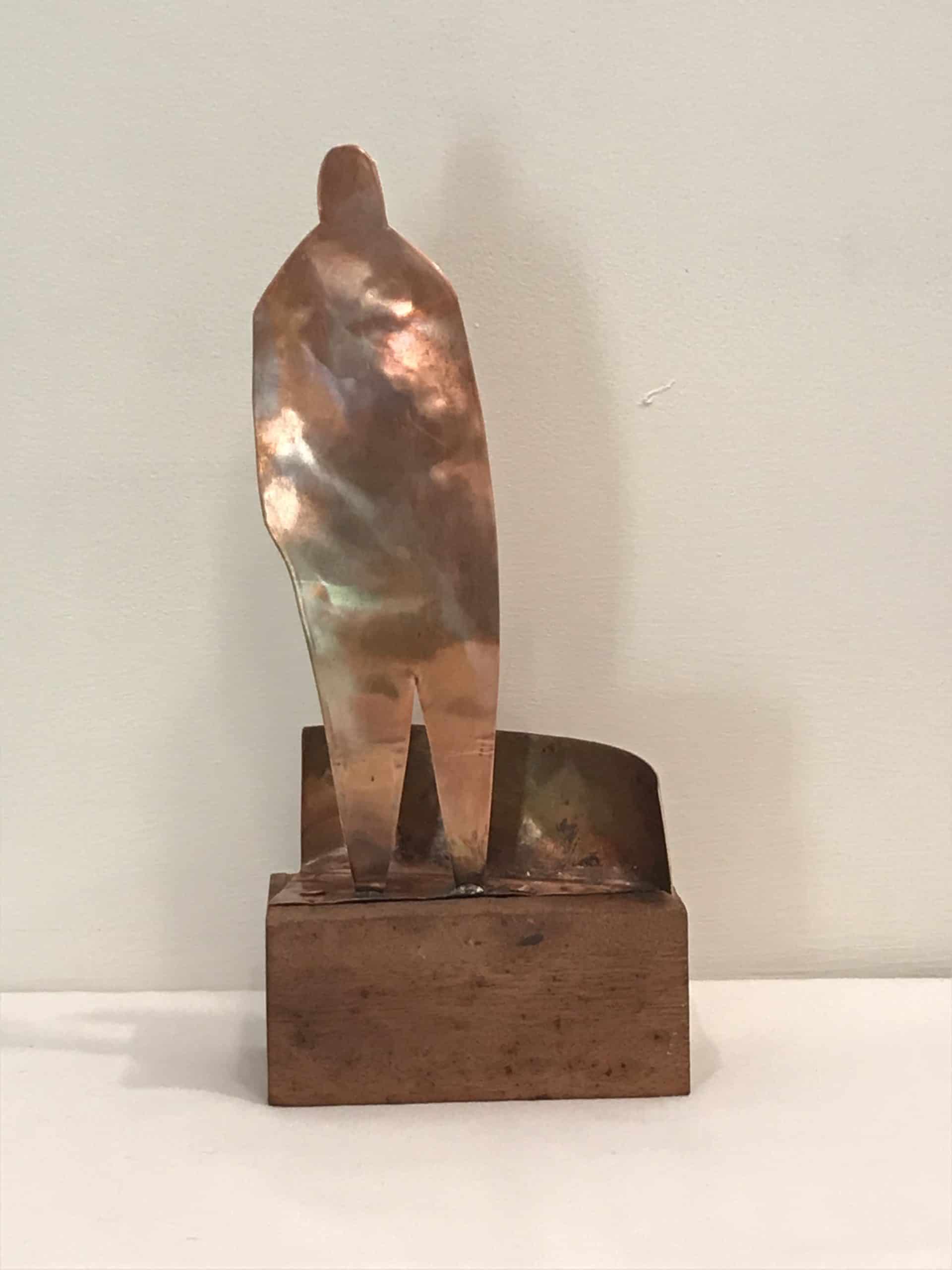 A copper and wood piece depicting a man standing on a curb.